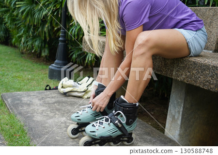 A woman is sitting on a bench and putting on her roller skates 130588748