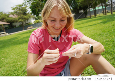 Young woman beading colorful bracelets outdoors in a park 130588761