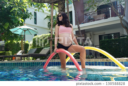 Pregnant young woman about to do exercises in pool with foam swim noodles 130588828