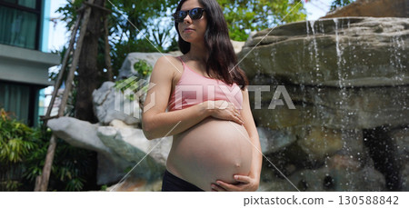 A pregnant woman is gracefully standing in front of a beautiful waterfall rock 130588842