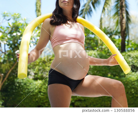Pregnant young woman about to do exercises in pool with foam swim noodles 130588856