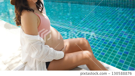 A pregnant woman in a pink bikini sits by a swimming pool A pregnant woman in a pink bikini sits by a swimming pool 130588876