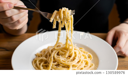 Elevated fork showcasing creamy pasta dish with parmesan and pepper served on a wooden table in a 130589976