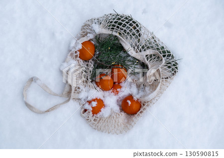 Ripe tangerines in reusable mesh bag with fir branch outside in snowy winter. Concept of sustainable Christmas celebration, responsibility and inclusivity. Oranges 130590815