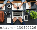 Overhead view of multiple people collaborating on laptops, tablets, and smartphones on a modern dark office desk, ideal for business, technology, and teamwork-related content. 130592126