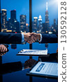 Two business professionals shaking hands over a contract document on a reflective desk in a modern high-rise office with a blurred city skyline at night, perfect for illustrating partnership, success, 130592128