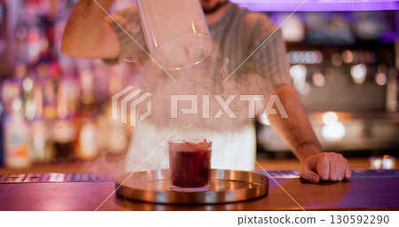 Bartender show. Drink presentation. Male barman lifting glass cylinder hood from smoke red alcoholic cocktail. Cool steam pub technique. Bartender show. Drink presentation. Male barman lifting glass cylinder hood from smoke red alcoholic cocktail. Cool steam pub technique. 130592290