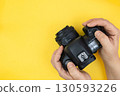 Digital camera in hands of photographer. Hands using digital camera on a yellow background with copy space for text. Top view, minimalism. 130593226