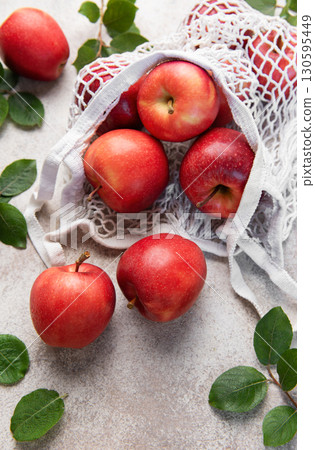 Fresh red apples spilling from reusable mesh bag on table 130595449
