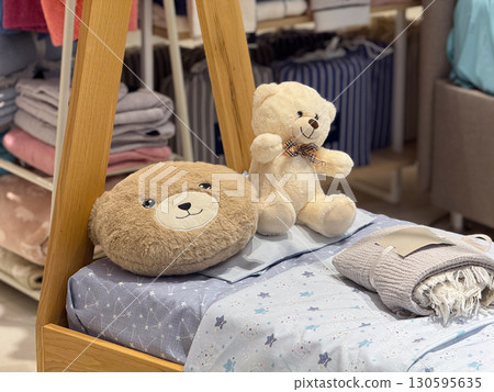 Soft toys and textiles on a children bed create a gentle sense of warmth and emotional comfort. Childhood, family care, consumer choice and playful atmosphere in a retail environment. 130595635