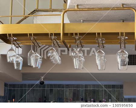 Hanging wine glasses in golden rack. Hospitality, bar equipment, and restaurant interior. 130595650