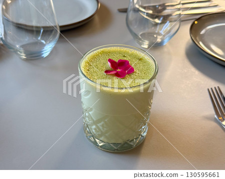 Glass of green matcha drink with edible flower. Refreshing beverage, garnish and modern presentation in cafe setting. Glass of green matcha drink with edible flower. Refreshing beverage, garnish and modern presentation in cafe setting. 130595661