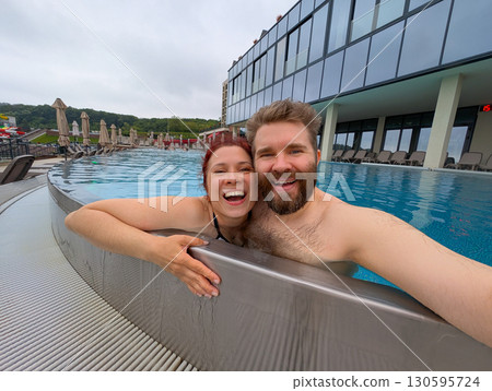 Couple smiling together in the pool. Love, bonding, and joyful summer vacation. 130595724