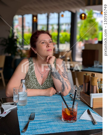 A woman sitting at a restaurant table with a cocktail. Lifestyle, dining, creativity, and relaxed urban atmosphere. 130595749