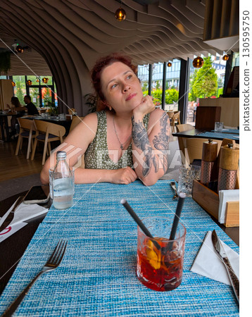A woman sitting at a restaurant table with a cocktail. Lifestyle, dining, creativity, and relaxed urban atmosphere. 130595750