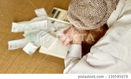 An elderly woman worried in front of a calculator and receipt _ left facing diagonal 130595878