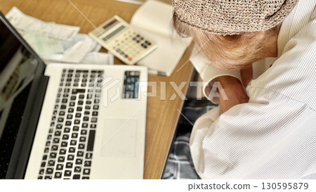 Elderly woman with her arms folded in front of a PC, calculator and notebook _ facing left 130595879
