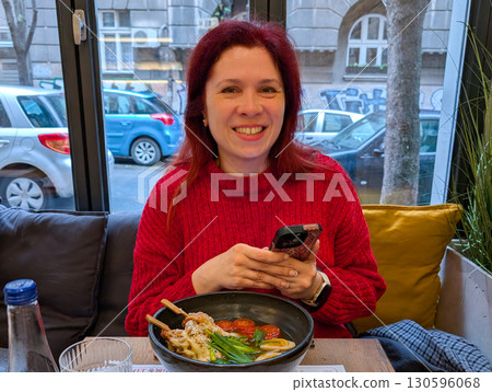 Woman smiling with ramen bowl on restaurant table. Joyful dining, food culture, and lifestyle moments with Asian cuisine. Woman smiling with ramen bowl on restaurant table. Joyful dining, food culture, and lifestyle moments with Asian cuisine. 130596068