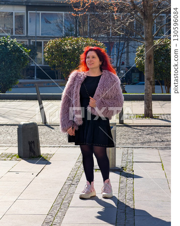 A woman in a purple fur coat and black dress stands on a sunny city street. Fashion identity, urban lifestyle, beauty, confidence and clothing trend in modern culture. 130596084