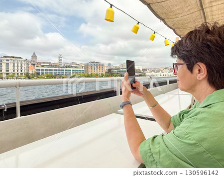 Woman photographing cityscape from ferry deck. Travel, tourism, and lifestyle on Bosphorus in Istanbul. Woman photographing cityscape from ferry deck. Travel, tourism, and lifestyle on Bosphorus in Istanbul. 130596142