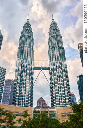 Nov 20, 2019 - Kuala Lumpur, Malaysia: Petronas Twin Towers with skybridge in urban skyline at day under dramatic cloudy blue sky. Scenic cityscape with lush park, modern Suria KLCC shopping mall in 130596433