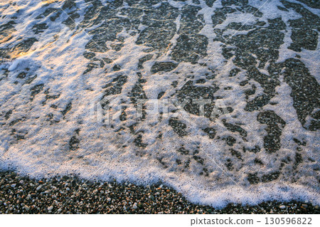 Ocean waves gently lapping against pebbled shore creating serene coastal atmosphere 130596822