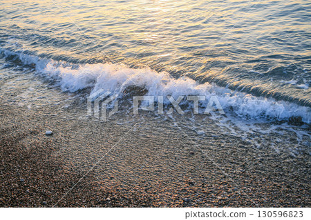 Gentle sea waves lapping against a pebbled shore during a serene sunset atmosphere 130596823