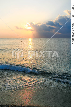 Serene sunrise over calm ocean waves reflecting golden light with soft clouds in the sky 130596830