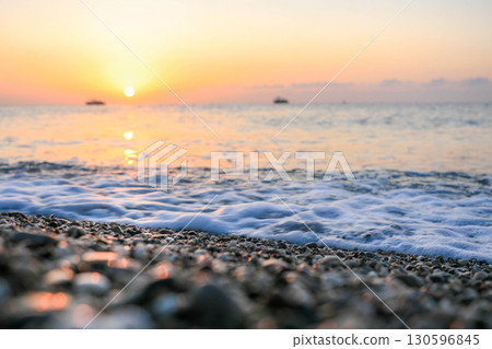 Serene beach scene at sunrise Gentle waves lapping against pebbled shore and colorful sky Soft focus 130596845