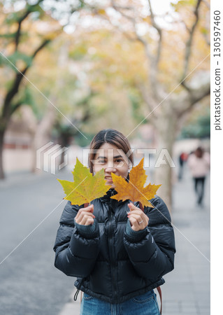 Female tourist holding yellow maple leaves and sightseeing on Anfu road in autumn. Woman traveler visiting Shanghai, China. Popular landmarks and tourist attractions in Shanghai. 130597460