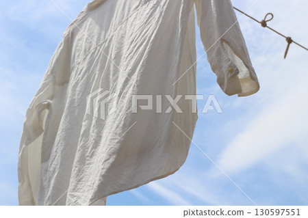 A single white shirt is hanging out to dry under the blue sky. A wrinkled shirt drying in the sun. 130597551