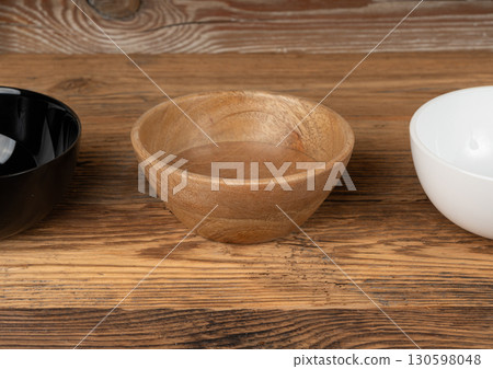 Three empty bowls on table, white porcelain, black and wooden dishes on tabletop, rustic dish Three empty bowls on table, white porcelain, black and wooden dishes on tabletop, rustic dish 130598048