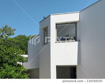 Modern white building with large geometric windows and clean minimalist lines under a clear blue sky 130598585