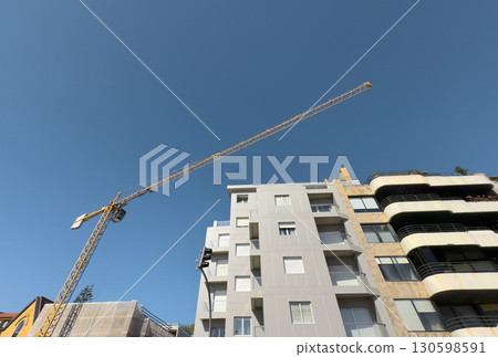 Modern apartment building under construction, with a tall yellow crane stretching across the clear 130598591