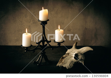 Beautiful vintage cast iron candelabrum with three burning candles and goats skull on the table in the dark. 130598804