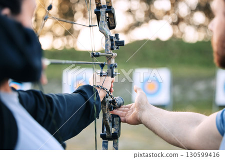 Archer hands, coach and bow or arrow learning for archery competition, athlete focus challenge or girl training practice. Teacher, teaching and man coaching woman on sports, aim and target shooting 130599416