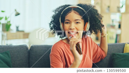 Happy woman on couch with headphones, dancing and singing in living room, relax with streaming radio. Music, energy and girl on sofa in home listening to audio with internet, technology and freedom. 130599500