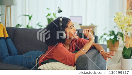Woman on sofa with earphones, phone and singing in living room, relax with streaming radio service. Music, energy and girl on couch in home listening to audio with internet, technology and headphones 130599517
