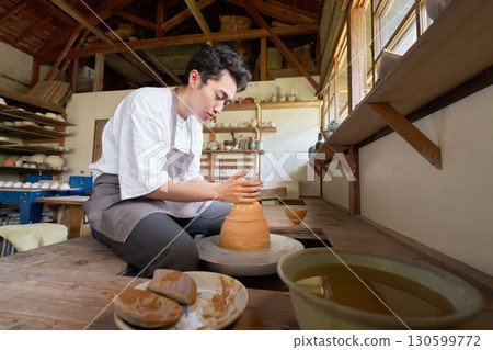 A young man shaping a pottery using a potter's wheel A young man shaping a pottery using a potter's wheel 130599772