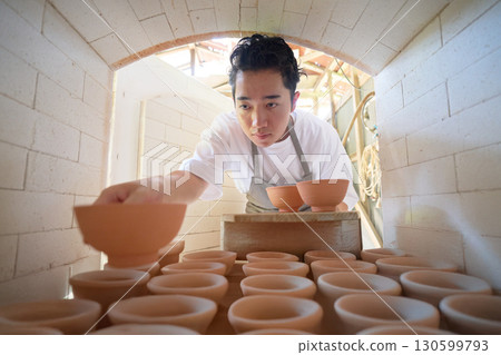 A young craftsman firing pottery into the kiln A young craftsman firing pottery into the kiln 130599793