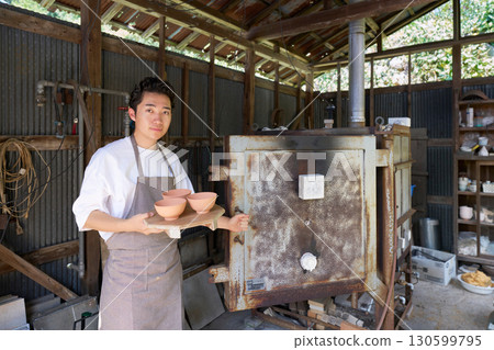 一位繫著圍裙的年輕陶工站在窯前 130599795