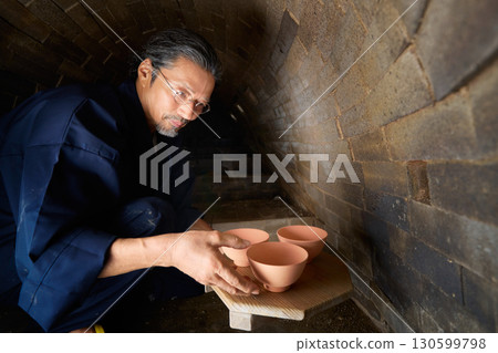 A potter arranging vessels in a kiln A potter arranging vessels in a kiln 130599798