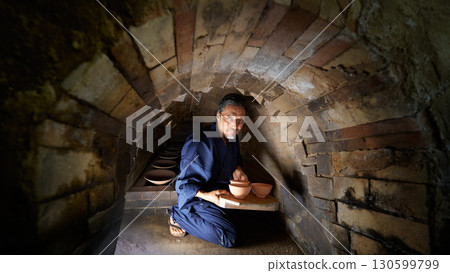 A senior man in traditional Japanese clothing working inside a kiln 130599799