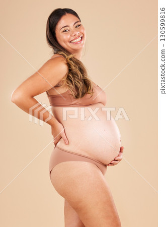 Portrait, pregnant and stomach with a model woman in studio on a beige background for motherhood. Baby, beauty and wellness with an attractive young mother in underwear for pregnancy or body health Portrait, pregnant and stomach with a model woman in studio on a beige background for motherhood. Baby, beauty and wellness with an attractive young mother in underwear for pregnancy or body health 130599816