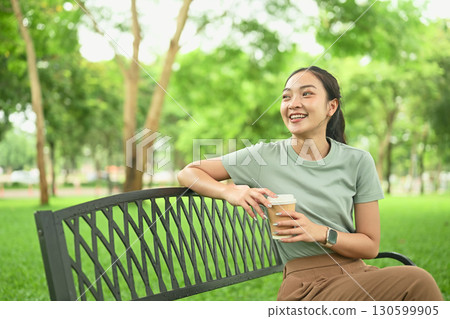 Happy female enjoying leisure time outdoors with a hot drink in hand Happy female enjoying leisure time outdoors with a hot drink in hand 130599905