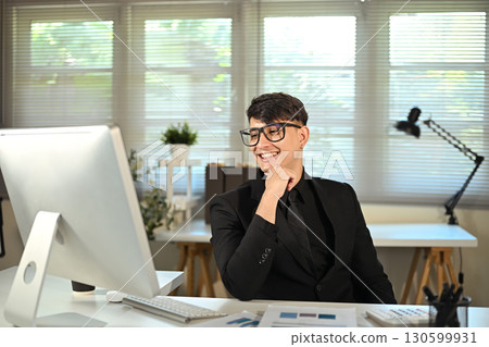 Smiling businessman in black suit working at desktop computer in modern office 130599931