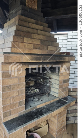 Outdoor brick barbecue oven with grill rack and ashes inside, surrounded by rustic wood and brick elements Outdoor brick barbecue oven with grill rack and ashes inside, surrounded by rustic wood and brick elements 130600152