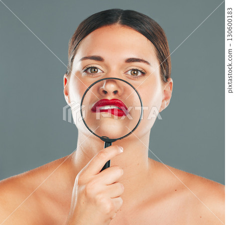 Portrait, magnifying glass and lips with a model woman in studio on a gray background for red makeup. Face, cosmetics or search with an attractive and funny young female checking her skin 130600183