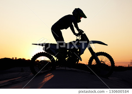 Silhouette, sports and motorcycle riding against sunset, sky and background in nature, extreme sport and adrenaline. Biking, motorbike and person driving on dirt road, sunrise and shadow or freedom 130600584