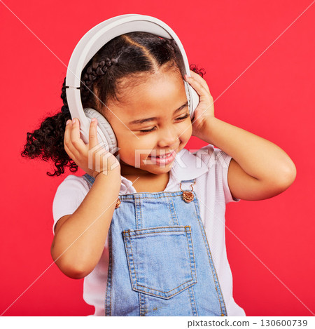 Happy, child and headphones for music, radio and fun podcast on isolated red background and dancing studio. Smile, little girl and kid listening to dance audio, song and streaming media on backdrop 130600739